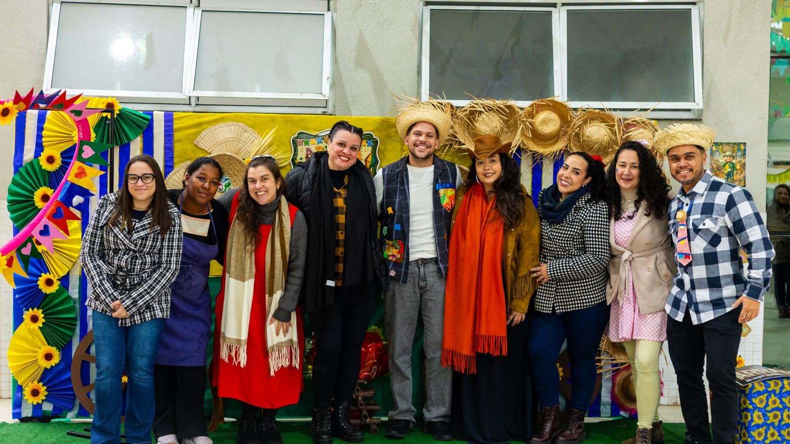 Grupo de participantes em trajes juninos reunidos diante do painel decorado da Festa Junina da APAE Barueri