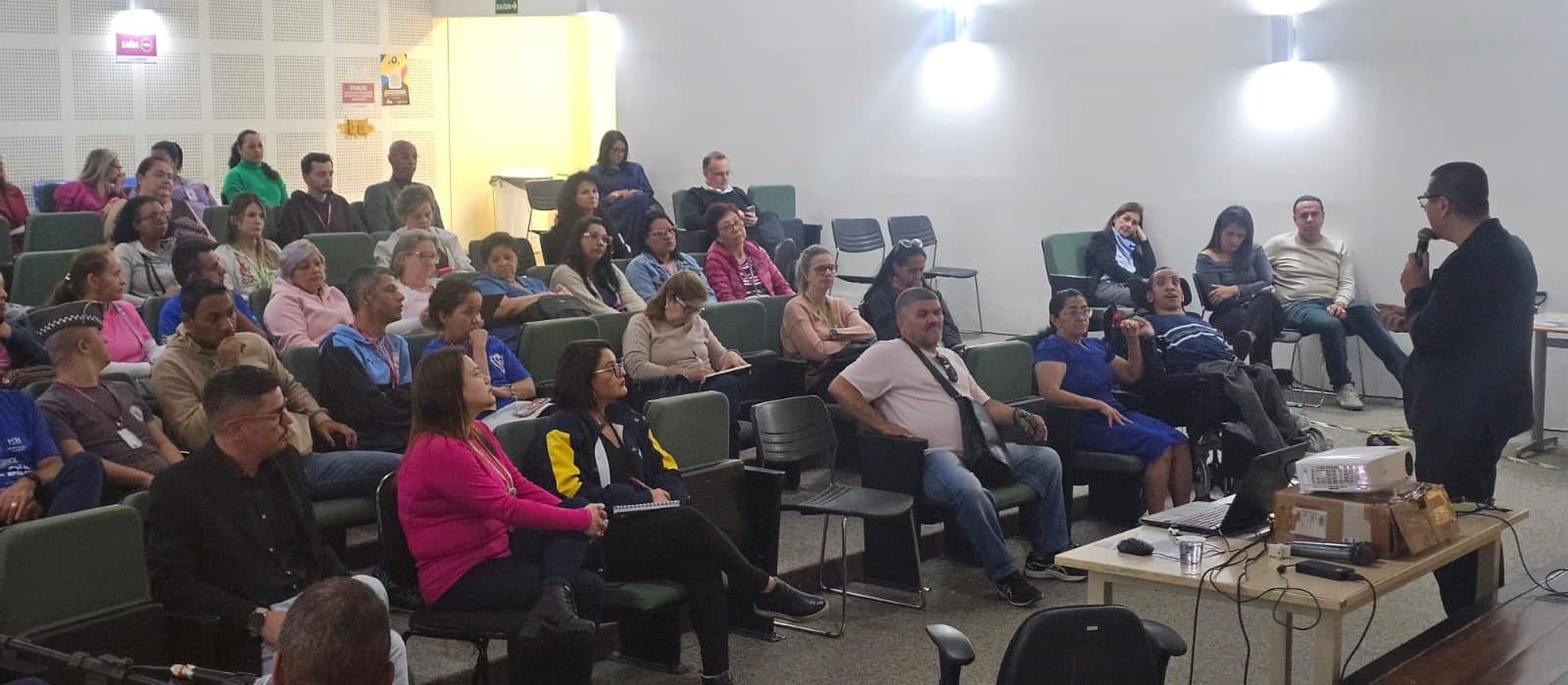 No auditório da SDPD, em Barueri, o presidente da APAE Barueri, Fagner Gouveia Bezerra, de terno escuro e óculos, fala ao microfone, de pé, à direita; diante dele, o plenário da reunião do Conselho Municipal dos Direitos da Pessoa com Deficiência acompanha sentado nas poltronas verdes, entre eles um homem em cadeira de rodas.