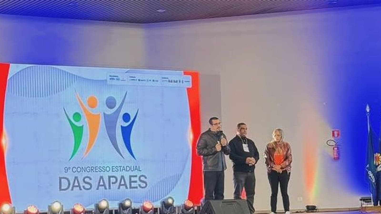 Participantes reunidos no palco do IX Congresso Estadual das APAEs, em Olímpia, diante do painel do evento