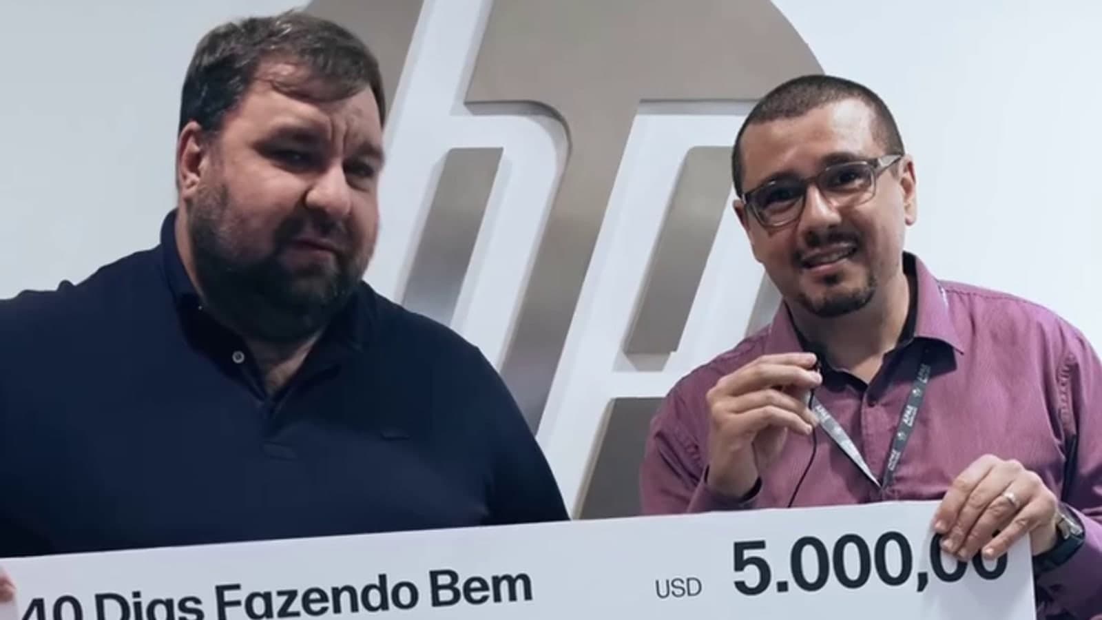 Presidente e vice-presidente da APAE Barueri seguram o cheque simbólico de US$ 5.000 do programa 40 Dias Fazendo Bem da HP, diante do painel da empresa